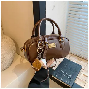 Brown Boston handbag featuring a metal label and cute baseball charm for casual styling.
