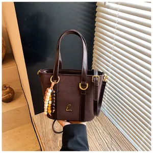 Close-up detail of the brown suede bucket bag with wooden bead charm and gold hardware.
