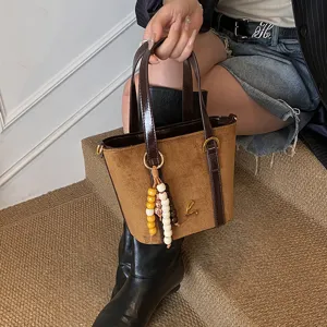 Stylish brown suede and PU patchwork bucket bag for women, featuring a chic top handle and charm.