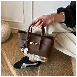 Detailed view of brown leather women handbag, elegant structured tote shoulder cross-body bag style.