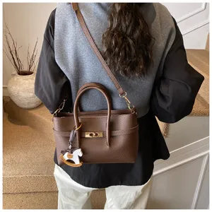 Detail view of brown leather handbag featuring turn lock closure and cute rocking horse charm.