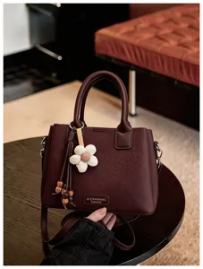 Detail shot of vintage burgundy shoulder bag with flower charm and tassel pendant on dark table.