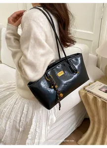 Elegante bolso de hombro negro con placa metálica, ideal para el estilo retro diario.