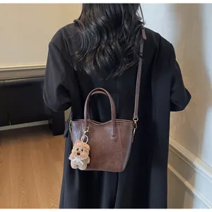 Detailed view of retro brown PU leather bucket bag with cute fluffy bear keychain pendant.