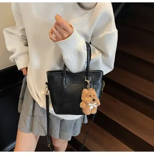 Close-up detail of the black bucket bag featuring metal hardware and a cute plush bear pendant.