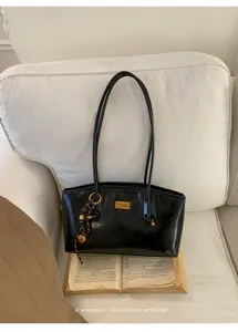 Detalle de bolso de hombro retro negro con dije metálico y estilo minimalista elegante.