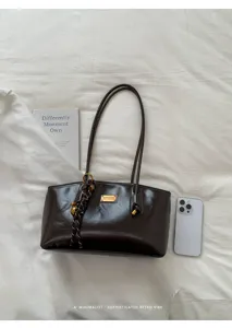 Vista detallada del bolso de hombro de charol marrón oscuro con herrajes elegantes y estilo retro.