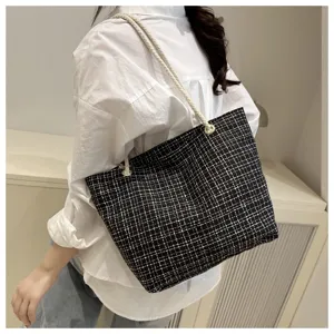 Detail shot of black and white plaid shoulder bag with rope handles worn on shoulder.