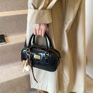 Versatile casual commuting black Boston handbag with baseball charm and metallic plaque detail.