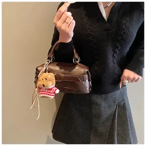 Detail shot of brown leather Boston handbag with cute plush bear keychain, stylish texture.