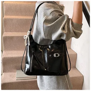 Detailed view of black patent leather shoulder bag with pearl bow pendant and front pocket.