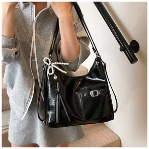 Detail view of black patent leather convertible shoulder bag with pearl bow and zipper.