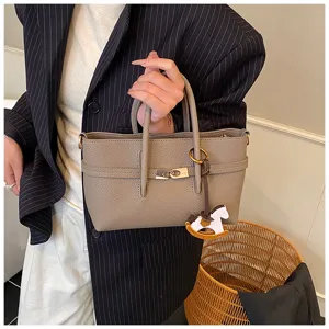 Close-up detail of grey leather top handle handbag with elegant metal lock and cute charm for women.