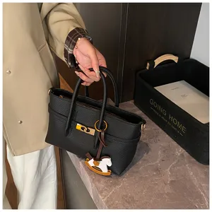Detailed view of black textured leather handbag with metal clasp and charm for stylish commute.
