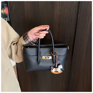 Detailed view of black textured handbag with metal lock and cute rocking horse charm.