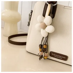 Close-up detail of white bucket bag with fabric flower pendant and wooden bead decoration.