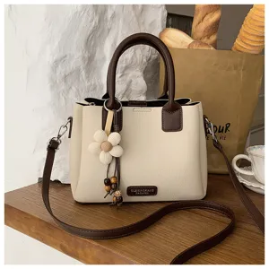 Close-up view of a stylish two-tone bucket bag with flower pendant and adjustable shoulder strap.