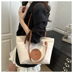Detail shot of white oxford cloth tote bag with brown leather handles and round fashion patch.