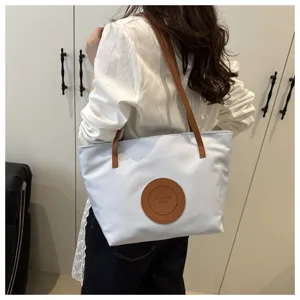 Oxford cloth shoulder bag detail view, blue tote with brown straps and round logo patch.