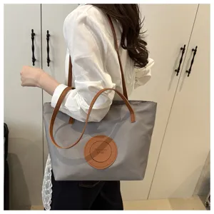Detailed view of grey oxford cloth women tote shoulder bag with brown straps and patch.