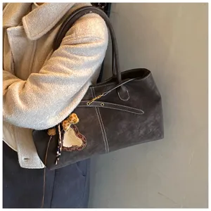 Detail shot of a dark brown suede tote bag featuring contrast white stitching and stylish charm.