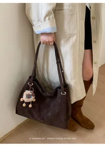 Detailed view of dark brown suede tote bag with cute sheep keychain, elegant outfit.