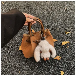 Detail view of a vintage brown bucket bag featuring a cute fluffy plush rabbit keychain.