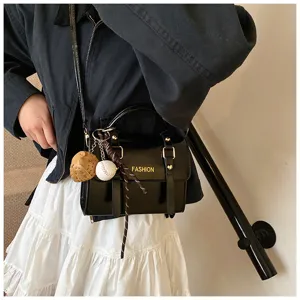 Vista detallada del bolso cruzado negro brillante para mujer con bonitos dijes de béisbol.