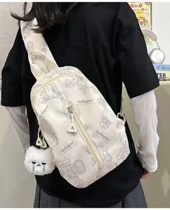 Detailansicht der beigen Schultertasche mit niedlichem Pluesschanhaenger und Baerendruck.