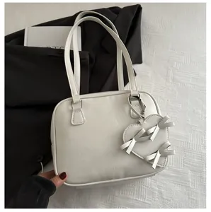 Detalle de bolso blanco de hombro con elegante colgante de lazo y textura de cuero.