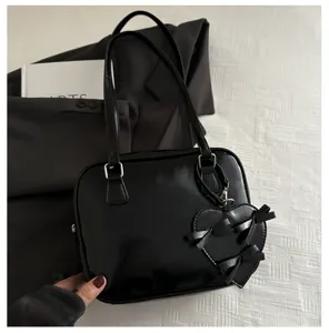 Detalle cercano del elegante bolso de hombro negro con bonito colgante de corazón y lazo.