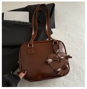 Detalle de bolso de hombro de cuero PU marron con colgante lazo de corazon y correas dobles.