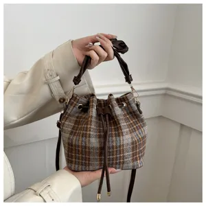 Stylish winter contrast color plaid bucket bag with PU leather handle and drawstring closure.
