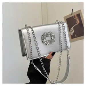 Close-up of silver metallic cross-body bag with sparkling crystal rhinestone buckle and chain.