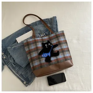 Detailed shot of the plaid tote bag with cute black cat embroidery and durable brown leather base.