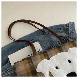 Plaid tote bag detail featuring white fluffy animal patch and brown leather handle design.