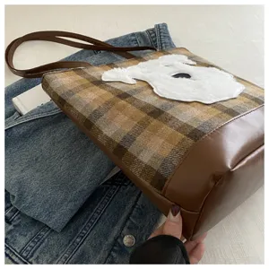 Close-up detail of the brown plaid tote bag featuring a cute fluffy white dog patch and base.
