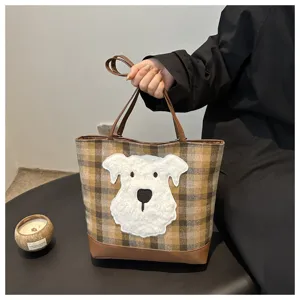 Detail view of a fashionable woolen plaid tote bag with cute white dog patch and brown leather.