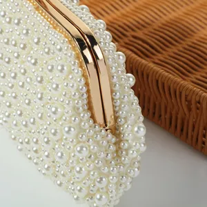 Close-up of elegant pearl-embellished evening clutch bag with glossy gold metal frame.