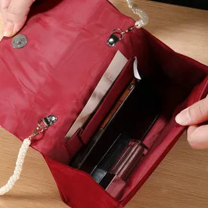 Red velvet evening bag interior detail showing spacious compartments, pearl strap and phone slot.