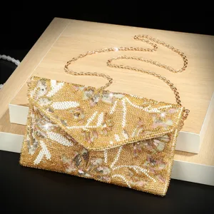 Detalle de bolso de noche tipo sobre con cuentas y lentejuelas doradas, elegante clutch con cadena.