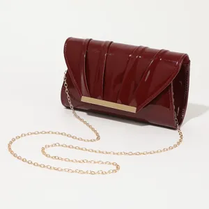 Elegant patent leather evening clutch bag detail showing pleated design and gold chain strap.