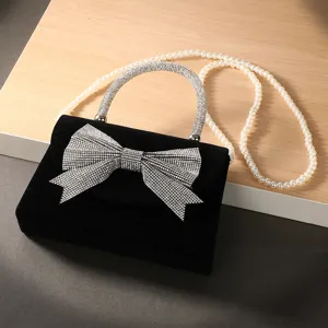 Details of black velvet evening bag featuring rhinestone bow, glitter handle and pearl strap.