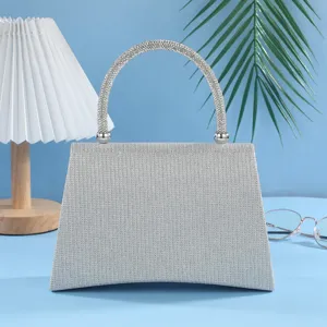 Detail view of sparkling silver rhinestone evening handbag with crystal handle on blue surface.