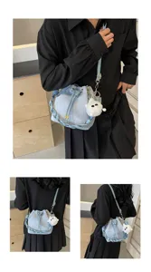 Primer plano detallado del bolso cubo azul claro con asa trenzada y colgante de felpa.