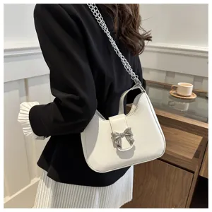 Witte schoudertas onder de arm met zilveren strikaccent en kettingriem, detailweergave.
