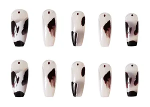 Primer plano detallado de uñas postizas con estampado de vaca, diseño salpicaduras, acabado brillante.
