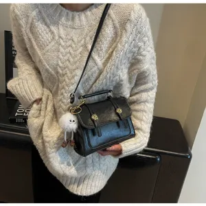 Klassieke zwarte schoudertas met stijlvolle metalen gesp en schattige pluche hangaccessoire.