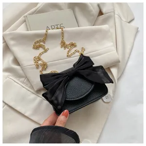 Black chic shoulder bag featuring an oversized sheer bow and gold chain, textured leather.