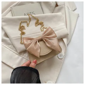 Close-up detail of the beige cross-body bag featuring a large satin bow and chic chain strap.